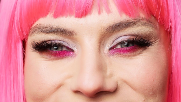 Macro colpo di donna positiva con trucco occhi colorato glamour e capelli rosa in posa in studio, divertirsi e sentirsi sicuri. Modello di bellezza sano e positivo con grandi ciglia. Primo piano estremo.