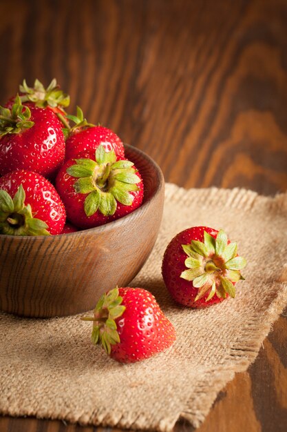 Macro foto della fragola rossa matura fresca in una ciotola di legno su fondo rustico. Prodotti naturali biologici