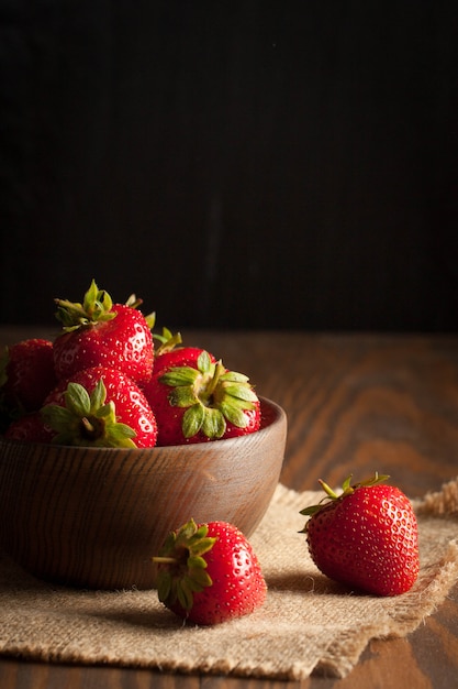 Macro foto della fragola rossa matura fresca in una ciotola di legno su fondo rustico. Prodotti naturali biologici