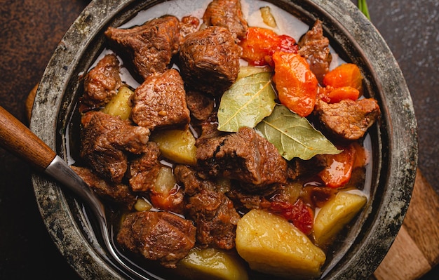 Macro primo piano dello stufato di manzo della carne con le verdure ed il sugo nella vista superiore della pentola rustica del metallo