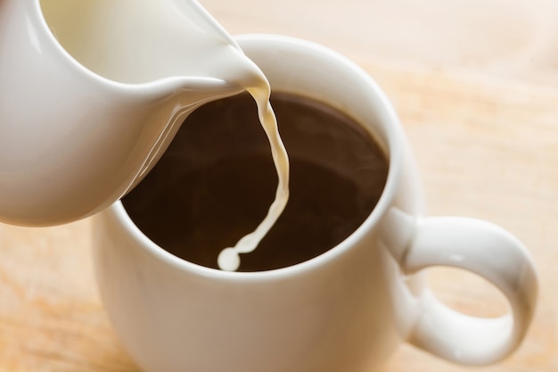 Macro sparare crema di versamento in una tazza bianca del caffè caldo di mattina.