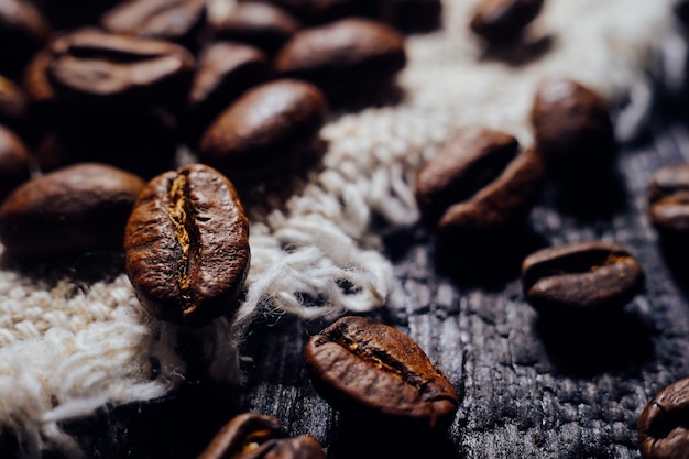 Macrofotografia di chicchi di caffè giacciono su legno strutturato e tela da imballaggio Caffè aromatico raccolto fresco Messa a fuoco selettiva