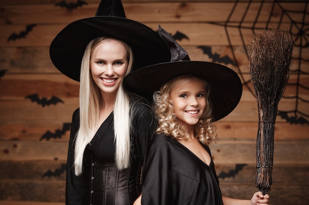 madre allegra e sua figlia in costumi della strega che celebrano posa di Halloween con le zucche curve