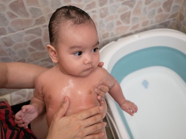 Madre asiatica che tiene piccola neonata sveglia e che fa il bagno suo figlio in bagno