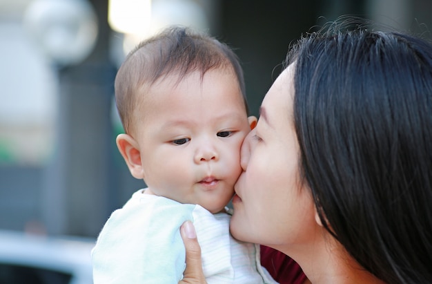 Madre asiatica del primo piano che bacia il suo infante. Famiglia felice