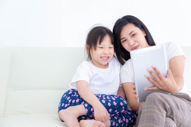 Madre asiatica e figlia piccola che utilizzano tablet digitale per guardare foto, video o leggere notizie. Concetti di famiglia e tecnologia felici.