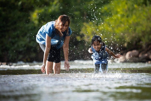 Madre asiatica e la sua ragazza del bambino che giocano nel fiume insieme al divertimento