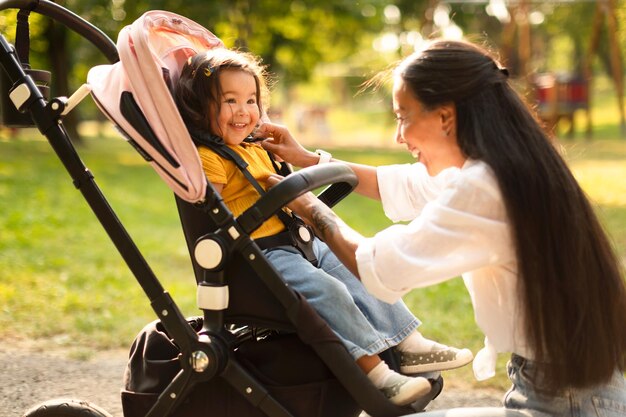 Madre asiatica felice che fa la figlia del bambino comoda in passeggino all'aperto