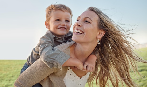 Madre bambino e felice sulle spalle durante le vacanze estive e il sole del cielo blu e giocare in un parco verde Madre felice bambino e sorriso divertendosi all'aperto per le vacanze con il sorriso ridere e amare nella natura