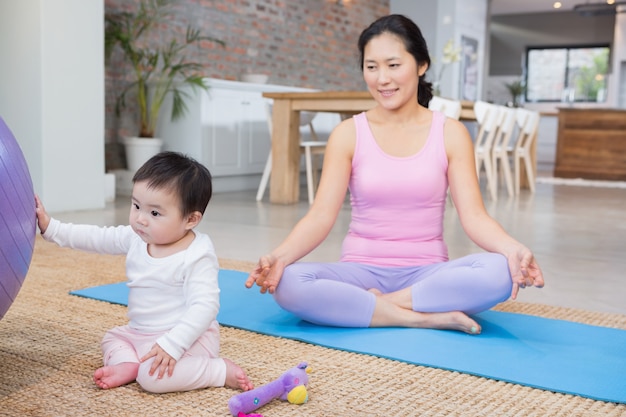 Madre calma che si siede sulla stuoia a casa mentre la figlia che gioca con la palla di forma fisica