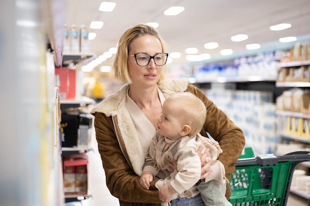 Madre caucasica che fa la spesa con il suo bambino bambino che sceglie prodotti nel reparto del supermercato