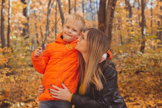 Madre che abbraccia il suo bambino durante la passeggiata nel parco autunnale stagione autunnale e concetto di genitore single