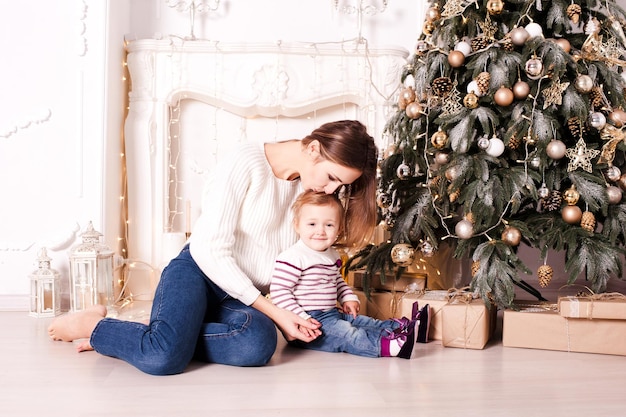 Madre che bacia la bambina seduta sotto l'albero di Natale