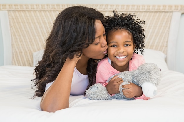 Madre che bacia la sua figlia sorridente sul letto