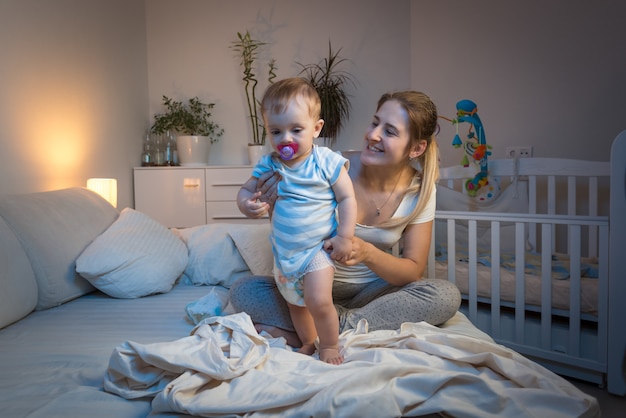 Madre che cambia i pannolini disordinati al suo bambino a letto di notte