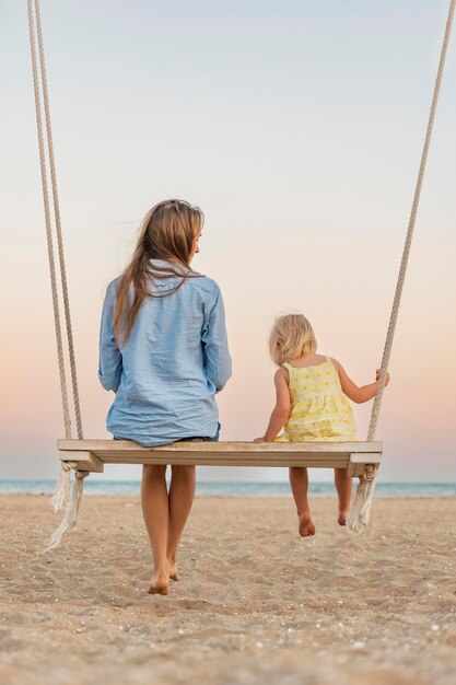 Madre che chiacchiera con la bambina sull'altalena e guarda lo splendido tramonto sul mare Alba magica sul mare