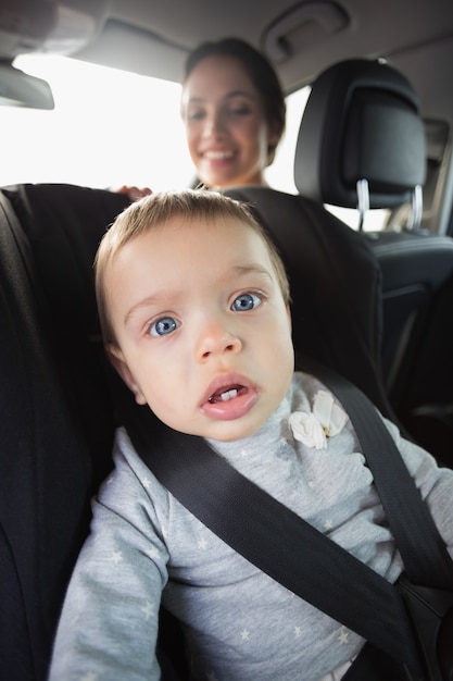 Madre che controlla il suo bambino nel seggiolino dell&#39;auto nella sua auto