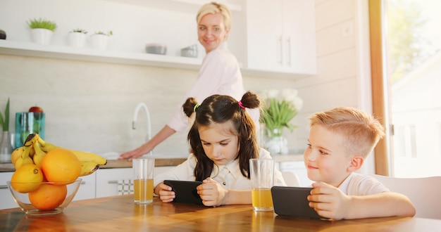 Madre che cucina insieme sorella e fratello che guardano video sul telefono cellulare insieme.