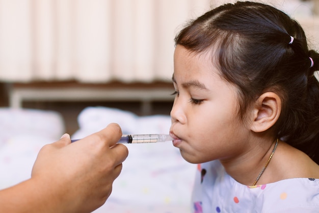 Madre che dà medicine a sua figlia. Ragazza ammalata del bambino asiatico che ottiene medicina liquida