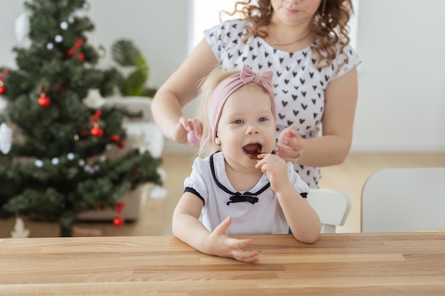 Madre che fissa l'apparecchio acustico dell'impianto cocleare della figlia sullo sfondo dell'albero di natale vacanze e concetto di diversità Tecnologie innovative