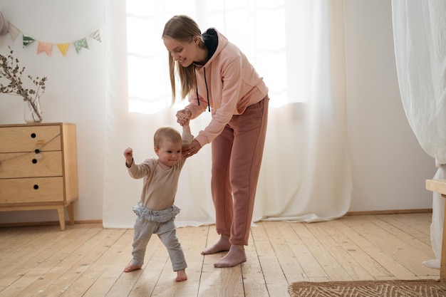 Madre che insegna a camminare con il suo bambino Ritratto di famiglia felice a casa concetto di primo passo