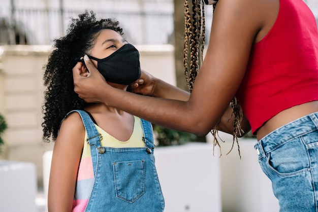 Madre che mette una maschera per il viso su sua figlia mentre si trova all'aperto sulla strada. Nuovo concetto di stile di vita normale.