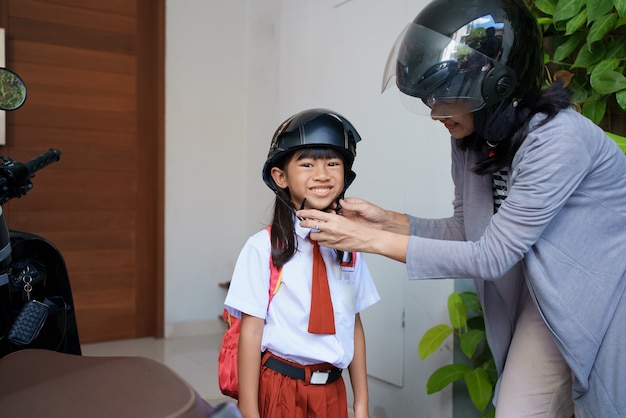 Madre che porta sua figlia a scuola in moto al mattino. studentessa primaria asiatica che indossa l'uniforme che torna a scuola