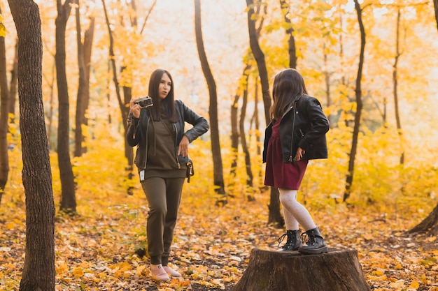 Madre che scatta una foto alla sua carismatica figlia con una fotocamera retrò in autunno parco hobby e tempo libero co