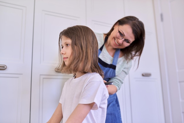 Madre che taglia i capelli alla figlia a casa, bambini, acconciature, capelli, bellezza.