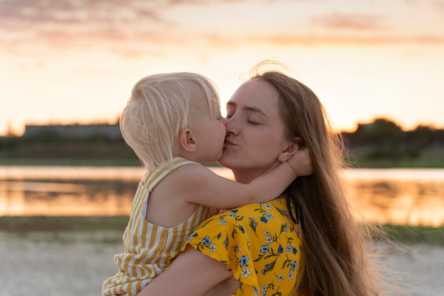 Madre che tiene il bambino e lo bacia dolcemente Madre e bambino in natura al tramonto