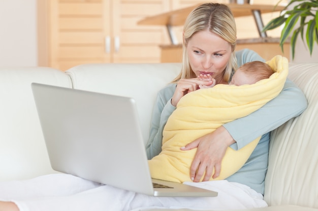 Madre che tiene il suo bambino mentre guardando il suo computer portatile