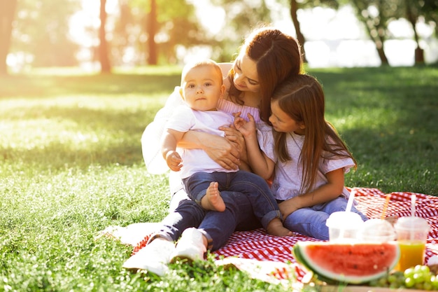 Madre che tiene piccolo figlio sulle mani con la figlia seduta vicino nel parco