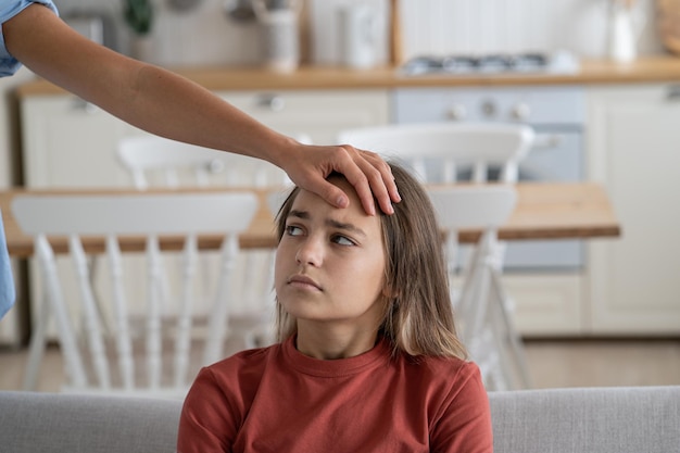 Madre che tocca la fronte della bambina malata seduta sul divano a casa controllando la temperatura