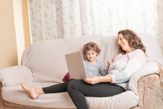 Madre che usa il portatile mentre è seduta accanto al figlio sul divano a casa