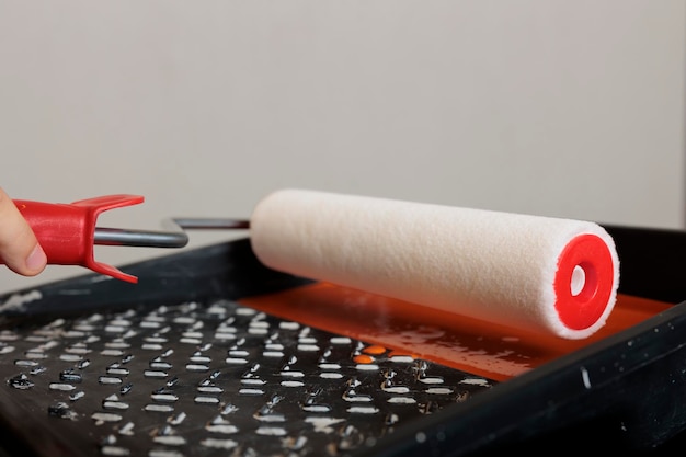 Madre che usa il rotolo di pennello e il colore arancione per dipingere le pareti dell'appartamento, lavorando sulla ristrutturazione della casa con strumenti di pittura e contenitore di tintura. Tenendo una spazzola rotonda con setole. Avvicinamento.