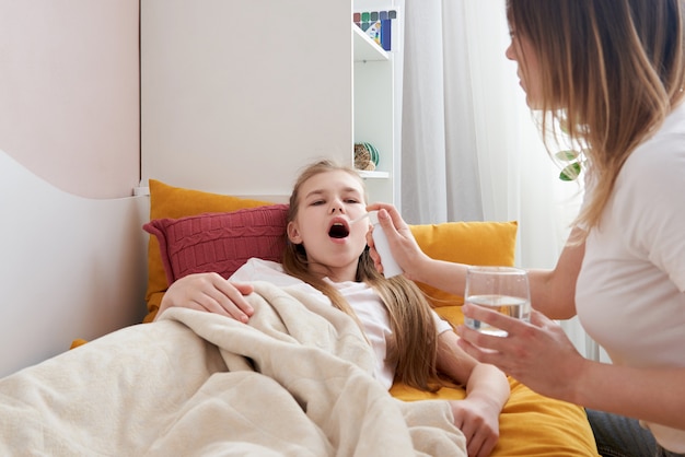 Madre che utilizza spray medico per la giovane figlia a casa, mal di gola