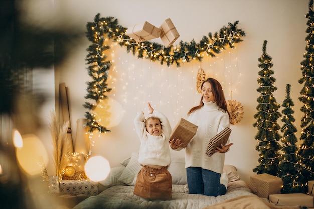 Madre con figlia che si diverte con i cuscini sul letto a Natale