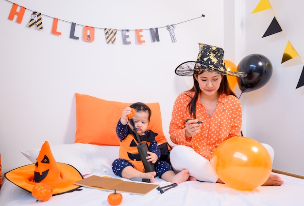 Madre con figlia in costume per festeggiare Halloween a casa. Bambino con la mamma alla decorazione della camera da letto nella stagione autunnale.