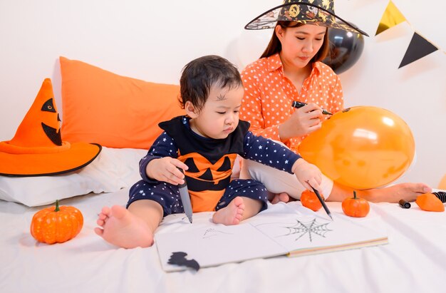 Madre con figlia in costume per festeggiare Halloween a casa. Bambino con la mamma alla decorazione della camera da letto per Dolcetto o scherzetto nella stagione autunnale.