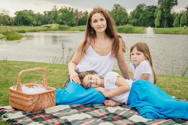 Madre con figlie giovani che hanno picnic. Famiglia con gli stessi vestiti vicino al lago