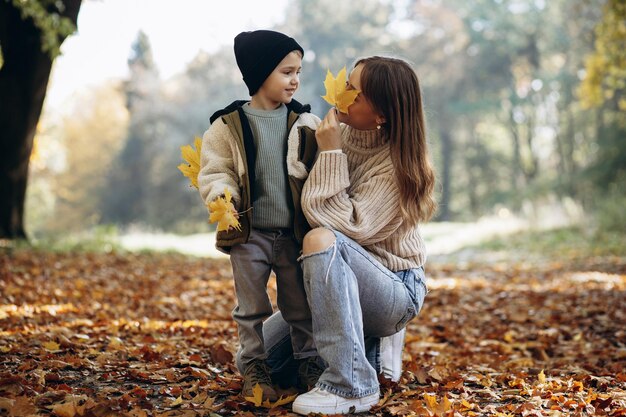 Madre con figlio che si diverte nel parco autunnale giocando con le foglie