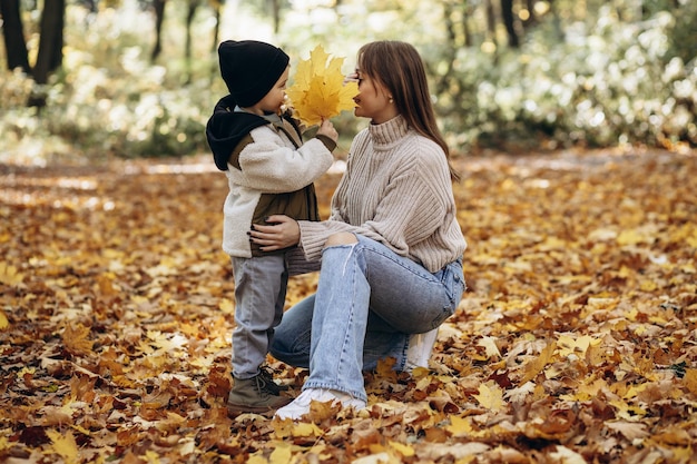 Madre con figlio che si diverte nel parco autunnale giocando con le foglie