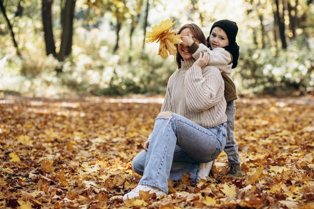 Madre con figlio che si diverte nel parco autunnale giocando con le foglie