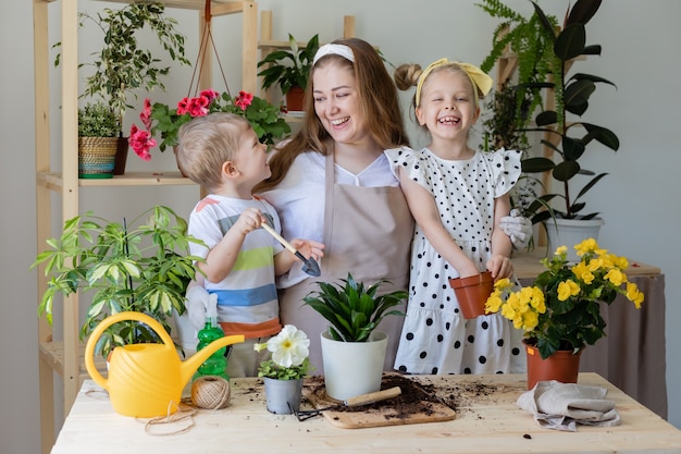 Madre con figlio e figlia in una pianta a digiuno o trapianta fiori al coperto Piccolo aiutante nelle faccende domestiche