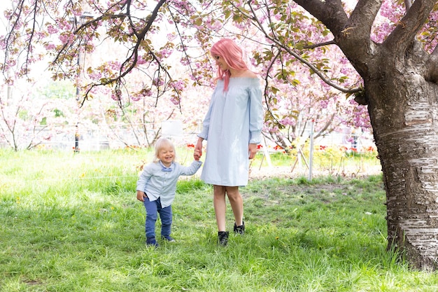 Madre con figlio piccolo nel parco che cammina vicino all'albero di sakura