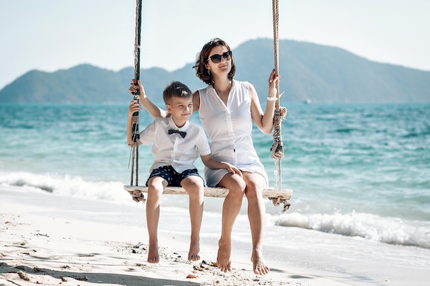 Madre con il suo bambino divertirsi oscillando in spiaggia tropicale. Phuket. Tailandia. Concetto di vacanza in famiglia