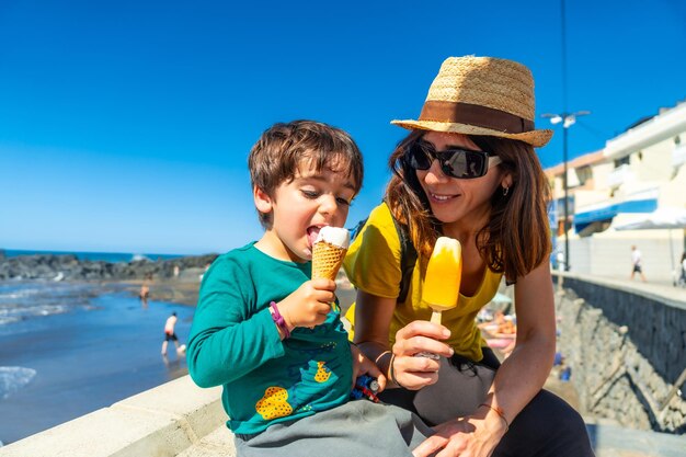 Madre con il suo piccolo figlio che si gode le vacanze estive mangiando gelato vicino al mare