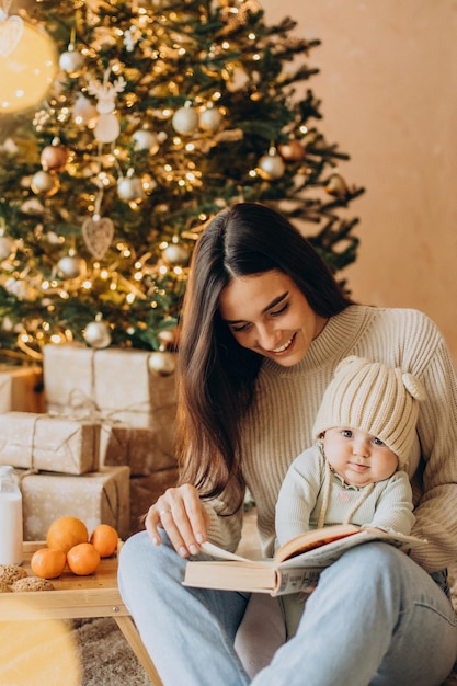 Madre con la sua bambina che legge un libro vicino all'albero di Natale