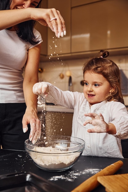 Madre con la sua piccola figlia che prepara il cibo in cucina e si diverte.