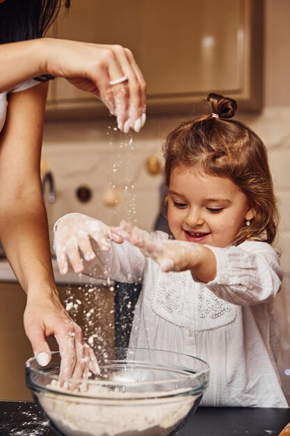 Madre con la sua piccola figlia che prepara il cibo in cucina e si diverte.